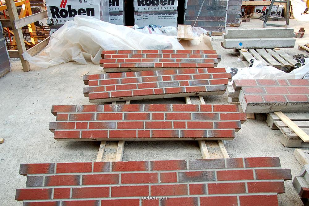 Rote Ziegel auf Holzpalette, Baustellenszene im Hintergrund.