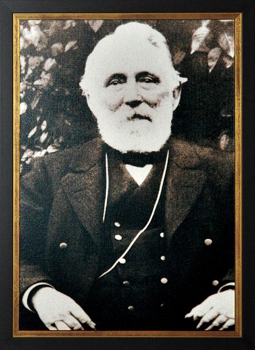 Älterer Mann mit Bart in Anzug, sitzt vor Bäumen, Schwarz-Weiß-Fotografie.