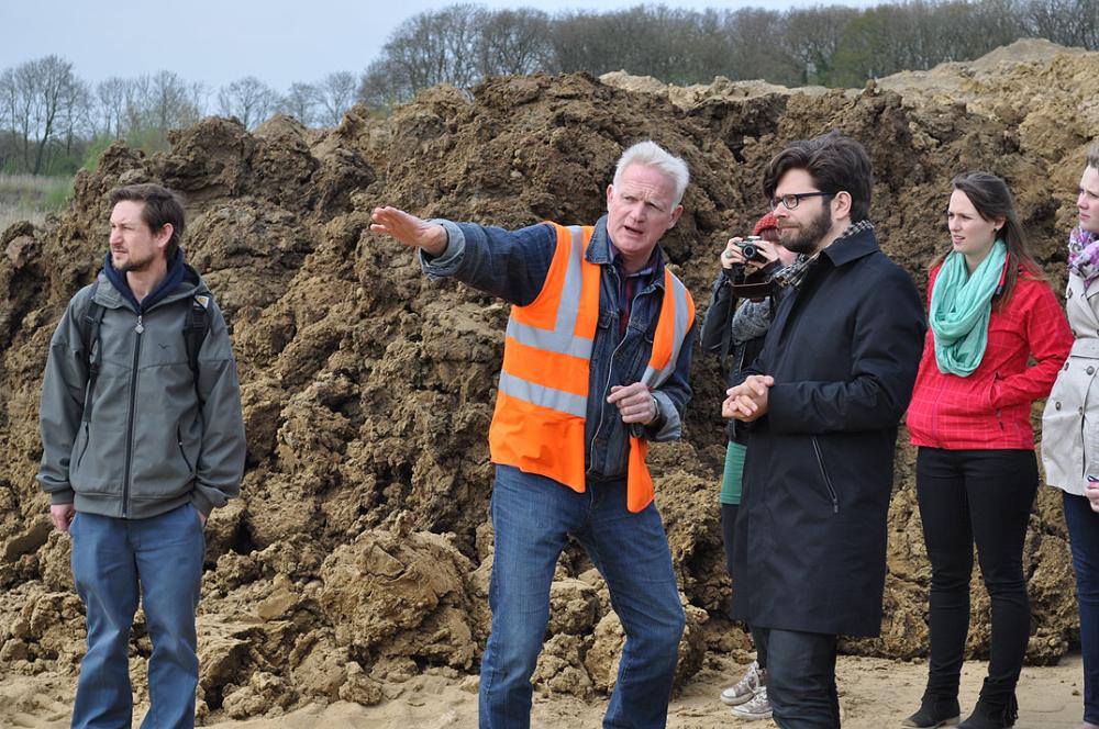 Gruppe Menschen bei Baustellenbesichtigung, einer trägt orange Warnweste.