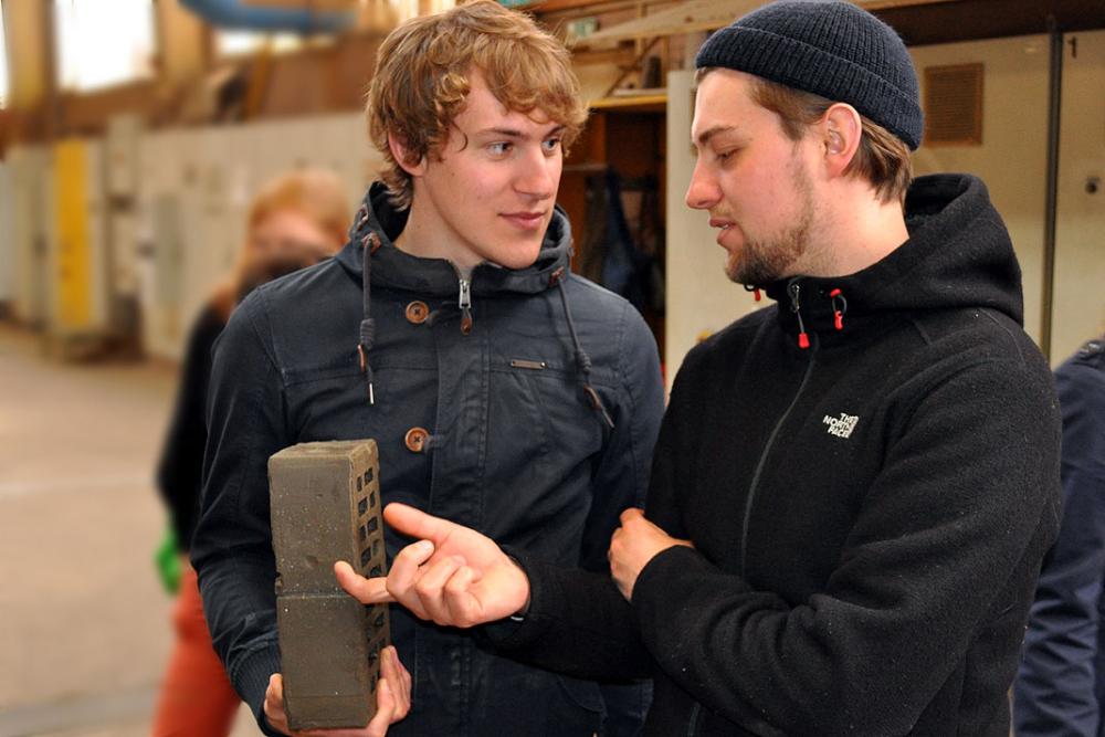 Zwei Männer diskutieren in einer Werkstatt und halten einen Steinblock.
