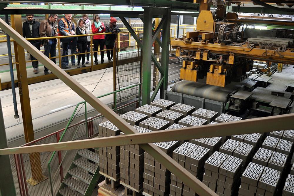 Fabrikarbeiter beobachten Maschinen, die gestapelte Metallblöcke bewegen.