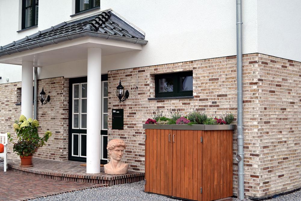 Hausfassade mit Backsteinwänden, weißer Säule und Pflanzen.