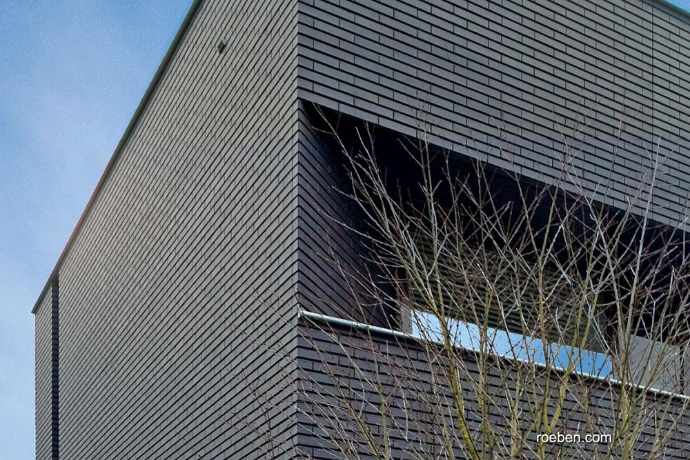 Eckansicht eines modernen Gebäudes mit Ziegelmuster, blauer Himmel im Hintergrund.
