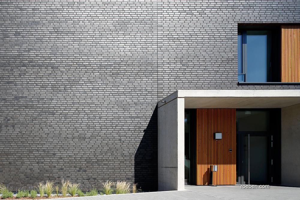 Moderne Fassade mit dunklen Kacheln und Holztüren.