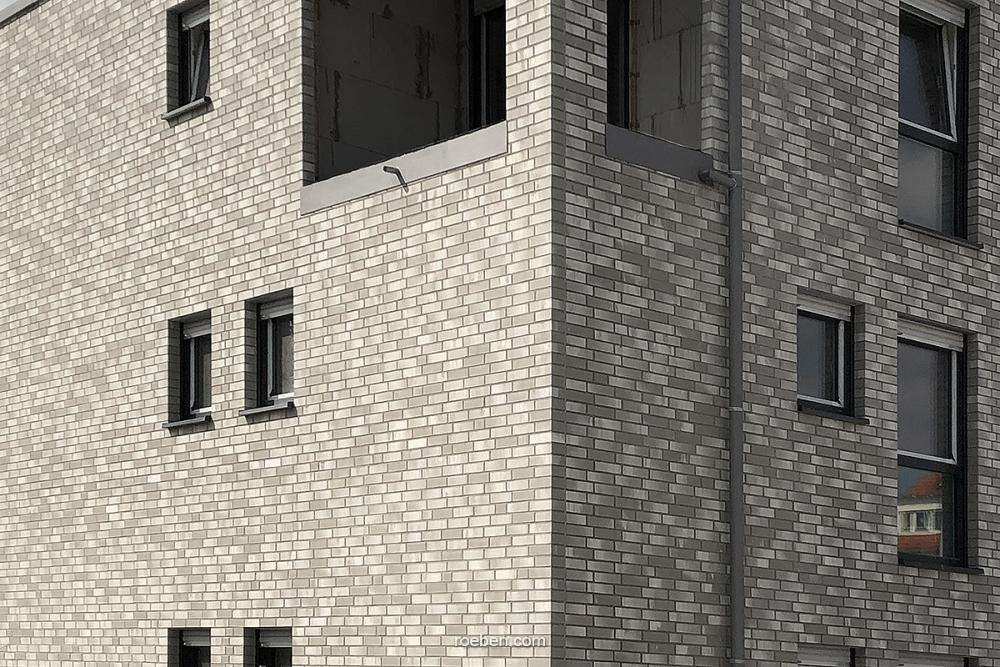 Graues Backsteingebäude mit mehreren kleinen Fenstern.