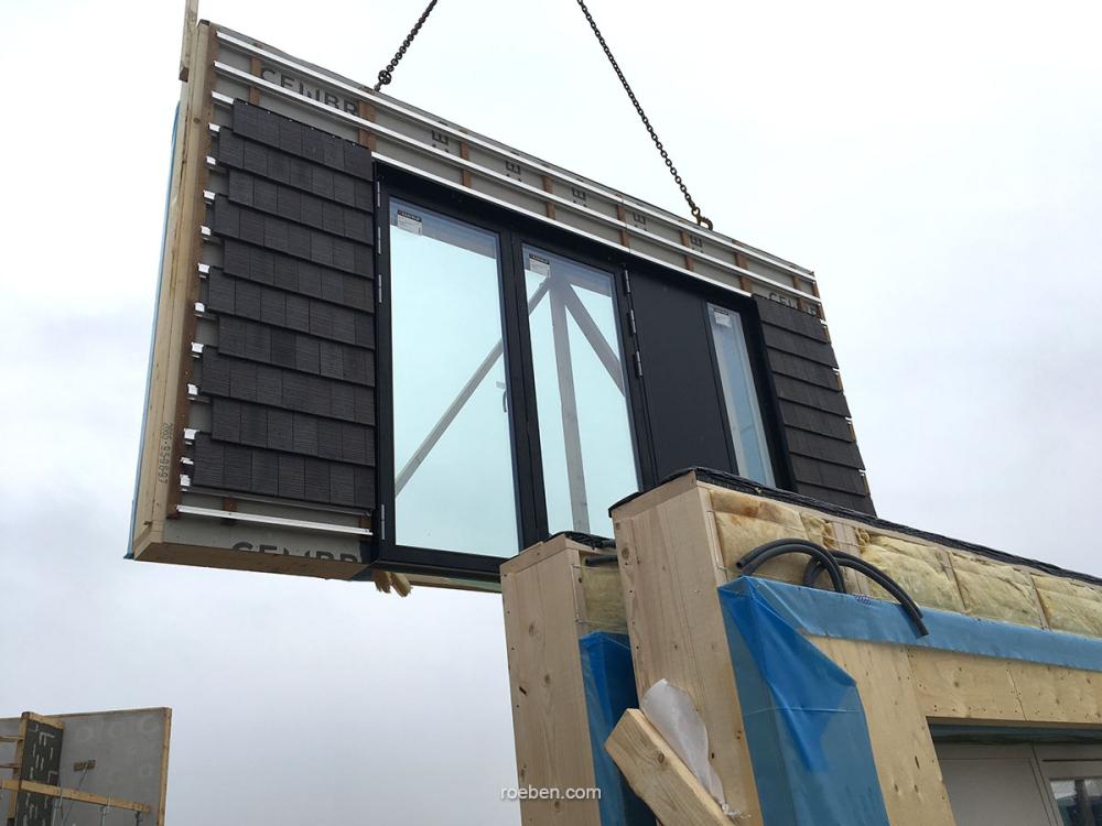 Fertige Wand mit Fenster wird auf Baustelle per Kran montiert.