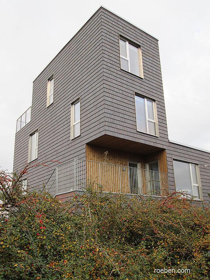 Modernes graues Würfelgebäude, umgeben von Büschen.