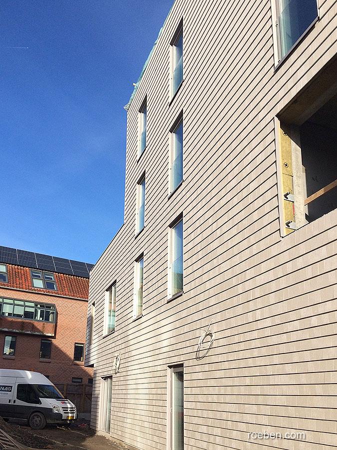 Mehrstöckiges Gebäude mit grauer Fassade und Fenstern, blauer Himmel.