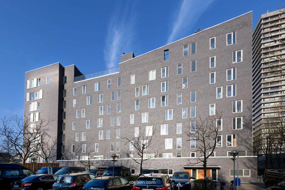 Sechsstöckiges graues Wohngebäude mit geparkten Autos davor.