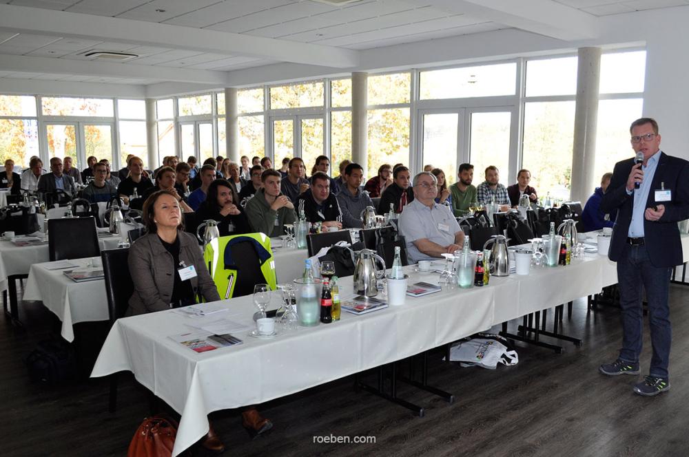 Konferenzraum mit Teilnehmern, Mann hält Vortrag.