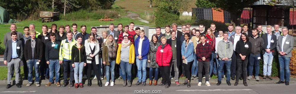 Gruppenfoto von Personen im Freien, verschiedene Kleidung, alle lächeln.