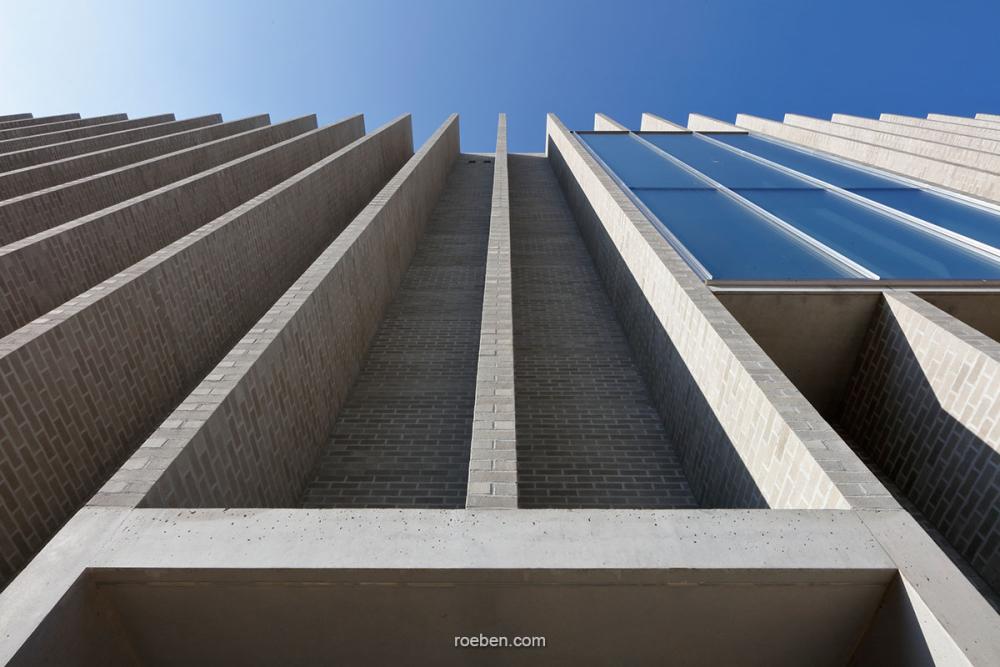 Brutalistisches Gebäude mit Betonfassade und Glas, blauer Himmel.