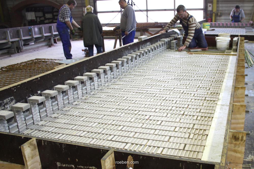 Fünf Personen arbeiten an einer großen Betonform in einer Werkhalle.