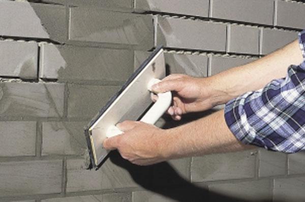 Hand trägt Zement mit Kelle auf graue Ziegelwand auf.